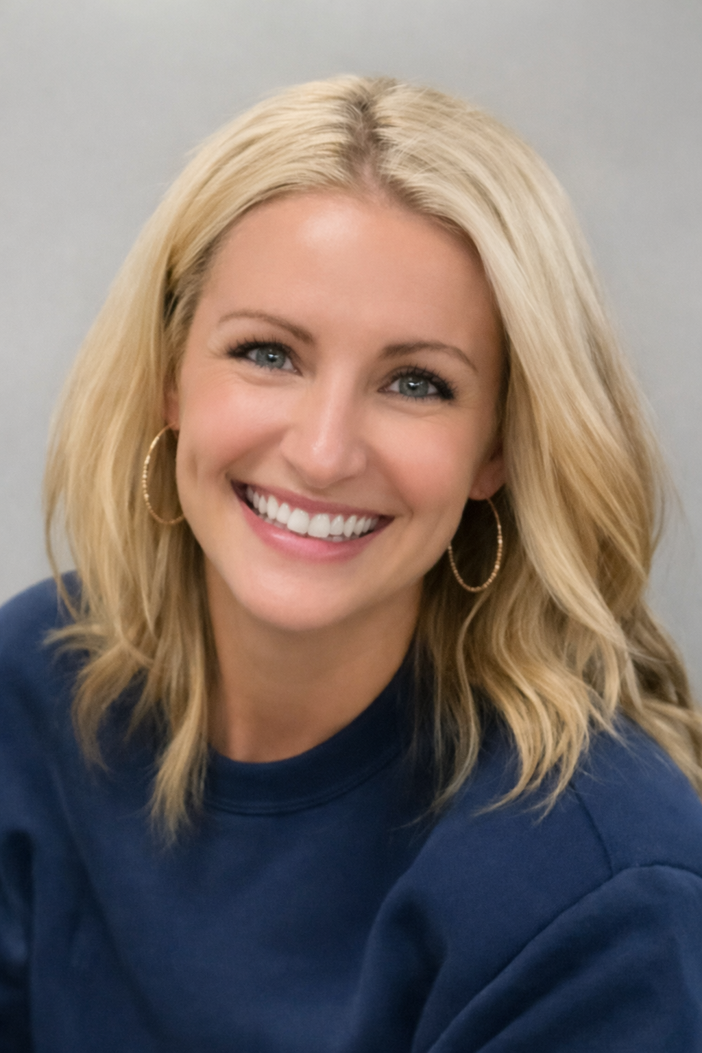 Smiling blonde woman with hoop earrings and blue top.