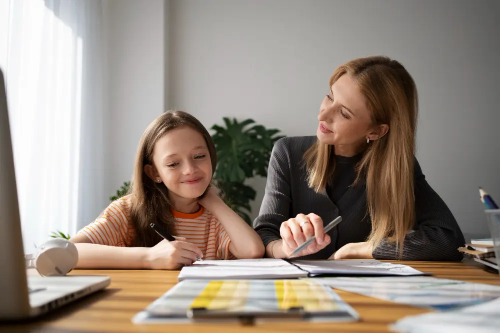 A mother helps her daughter with homework at a table.