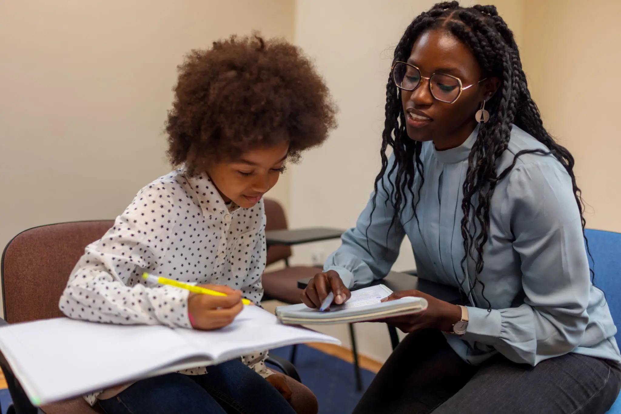 A woman helping a young girl with her homework at a desk.